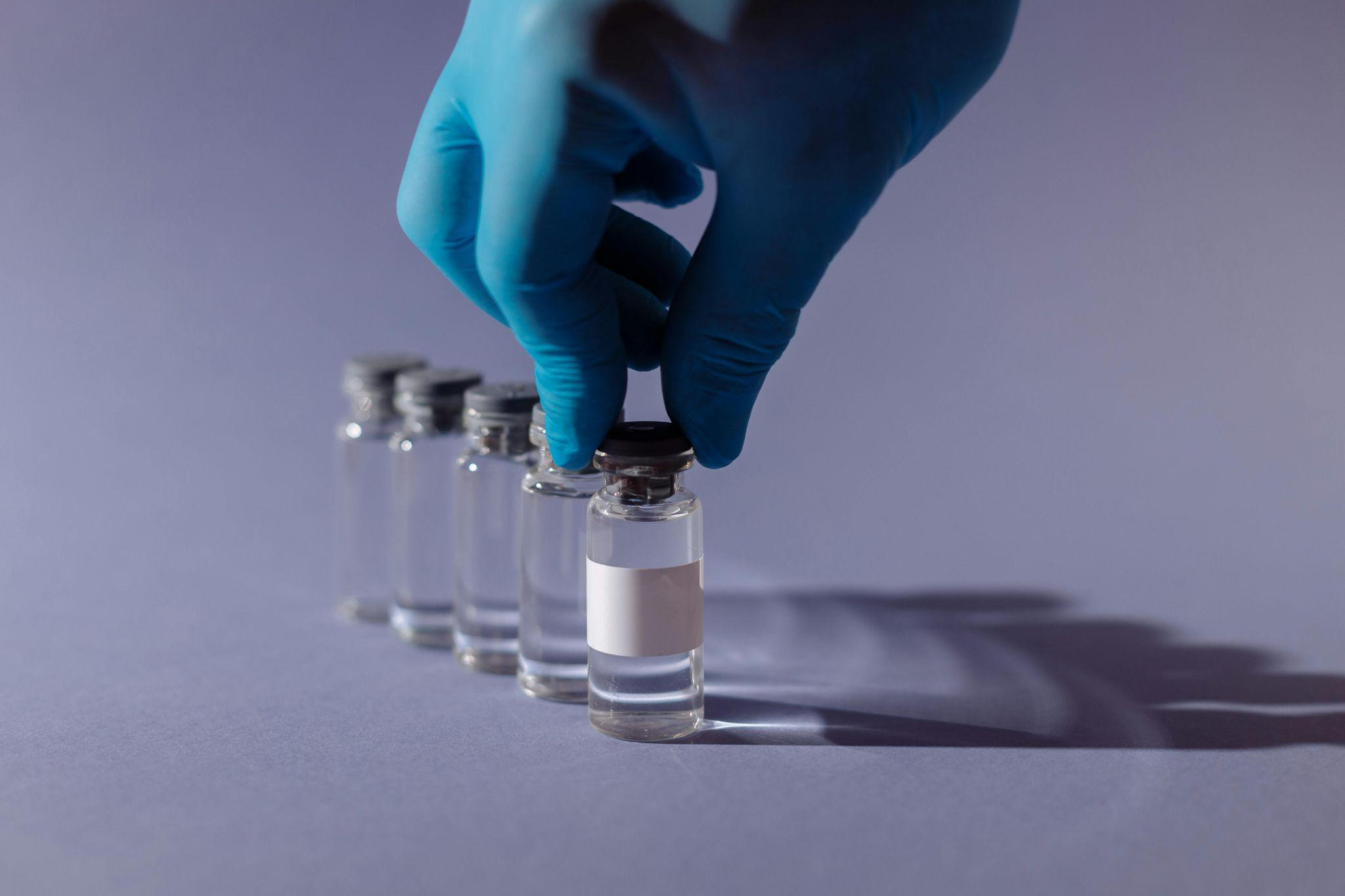 Hand in blue glove holding glass vial